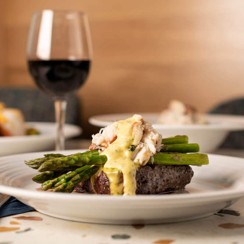Georgie's steak "Oscar Style" (topped with Fresh Dungeness Crab, Béarnaise, Asparagus). In the background is a glass of red wine.