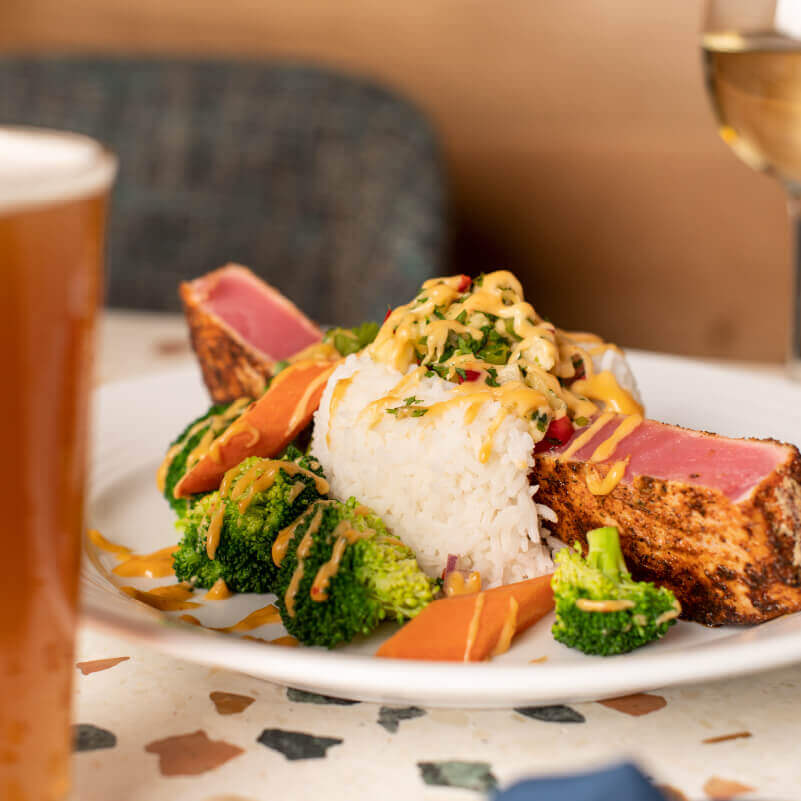Georgie's Blackened Ahi Tuna featuring a blackened Ahi steak seared RARE and topped with fresh pineapple-salsa. Served with fresh steamed vegetables and a sweet and spicy red curry cream sauce over Jasmine rice. The dish is served with a beer