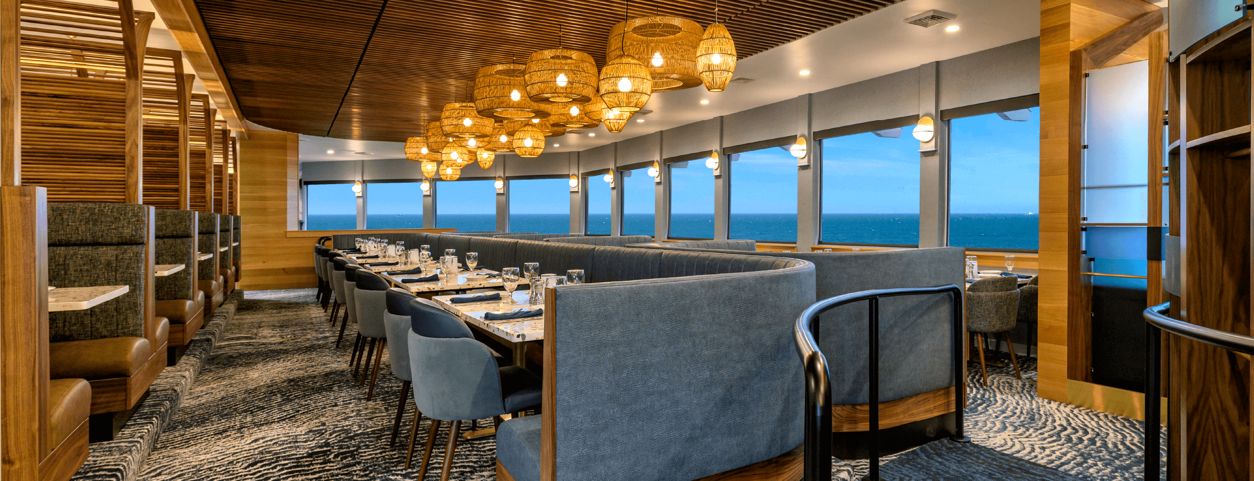 Georgie's restaurant interior featuring a full wall of windows looking over the Pacific ocean and rows of individual tables and booth seating.