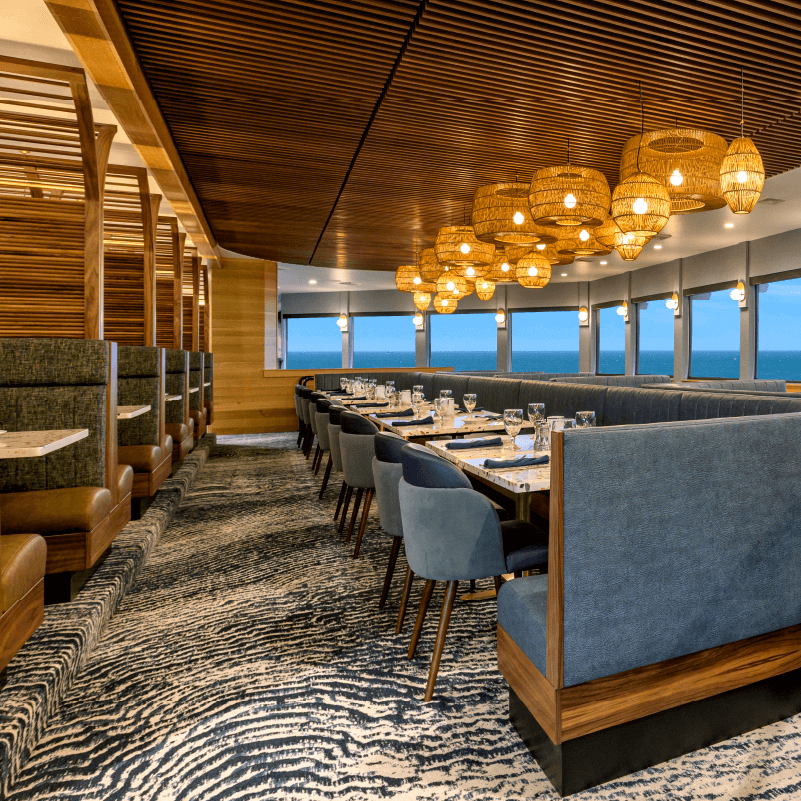 Georgie's restaurant interior featuring a full wall of windows looking over the Pacific ocean and rows of individual tables and booth seating.