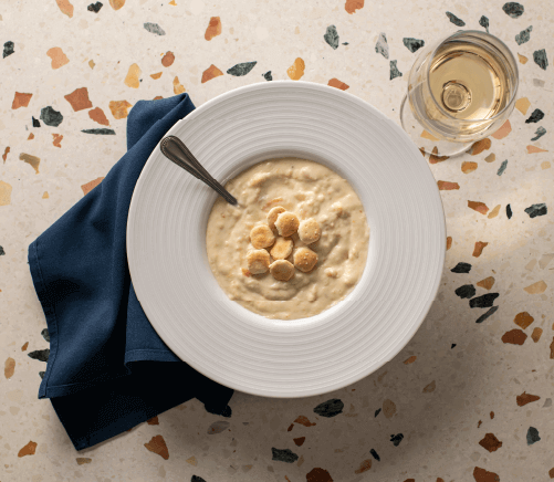 Georgie's New-England Clam Chowder in a bowl, topped with oyster crackers and served with a glass of wine.